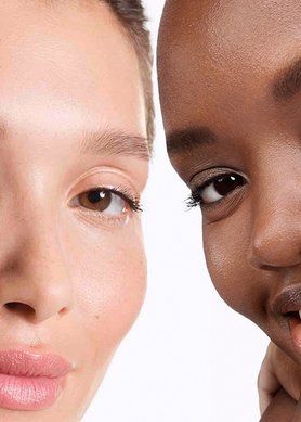 Two women smiling, with one applying a face cream to her cheek