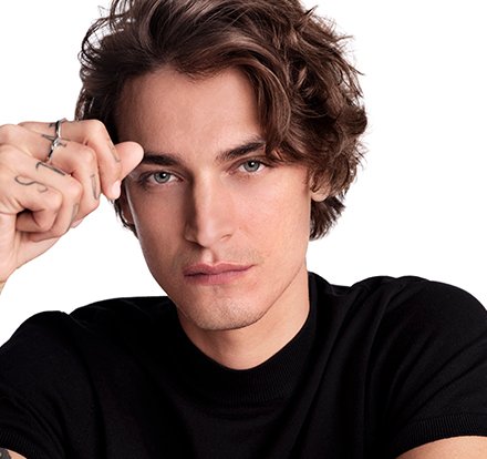 Man with wavey hair lifting his hand to his head