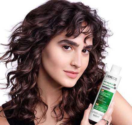 Woman with wavey hair holding Dercos 2 in 1