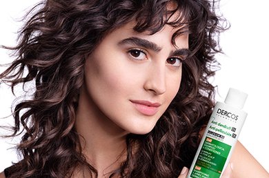 Woman with wavey hair holding Dercos 2 in 1