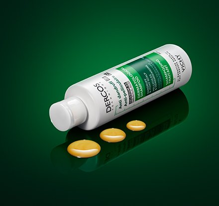 Dercos Anti-Dandruff Shampoo lying flat next to 3 droplets of product